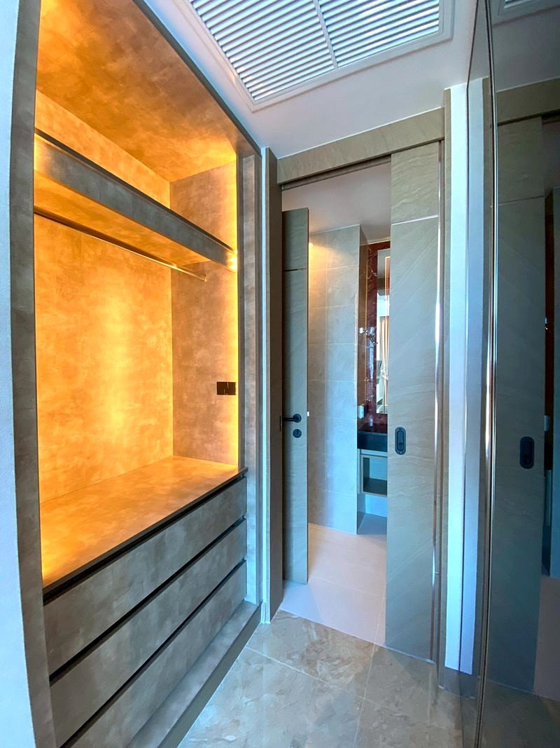 The_Riviera_Ocean_Drive_3214_6 Modern bathroom with a warm-lit built-in storage alcove on the left and a doorway to a marble-tiled bathroom ahead, visible through glass doors.