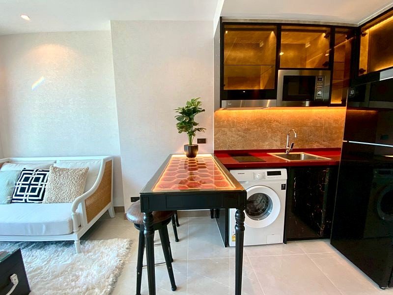 Open-concept living area with a white sofa, patterned cushions, and a black bar-height island in front of a modern kitchen.