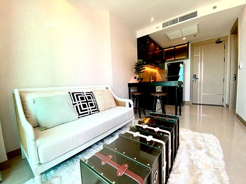 Modern living room with a white sofa and pastel cushions, a fluffy white rug, and a row of black suitcase-style coffee tables.