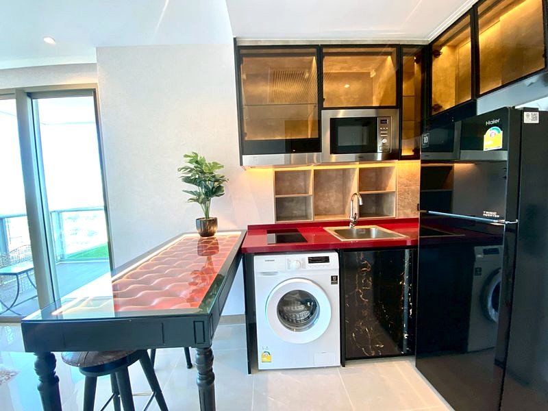 Modern kitchen with red countertop, black cabinets, washing machine, microwave, and a balcony view to the left.