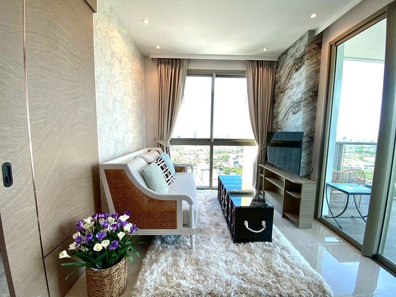 Bright living room with white and wicker sofa, fluffy white rug, and large balcony windows with natural light.