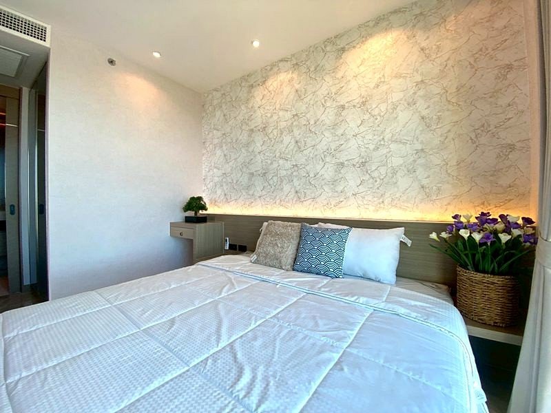 Bedroom with a large bed, white quilt, marble accent wall, warm LED glow, and potted plants on both sides.