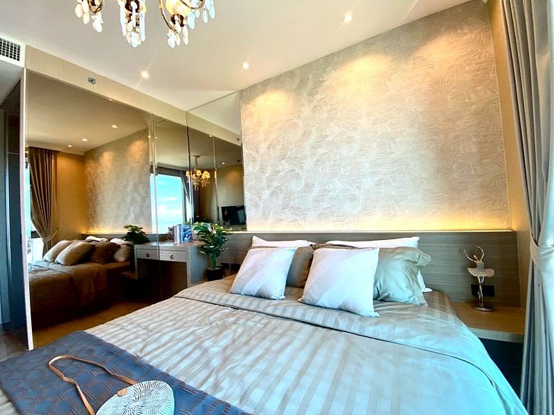 King-size bed with striped bedding in a stylish hotel room featuring a mirrored wall and chandelier