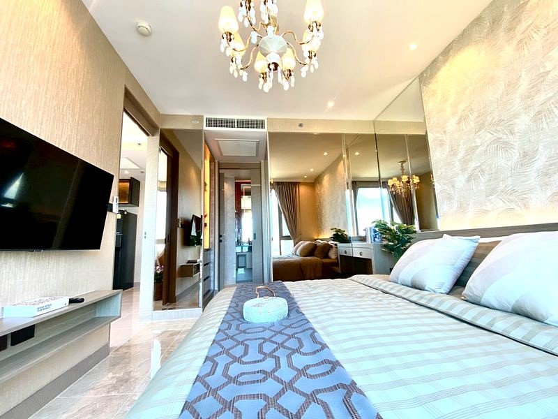 Hotel bedroom with a chandelier, large bed, and wall-mounted TV in a bright, modern suite.