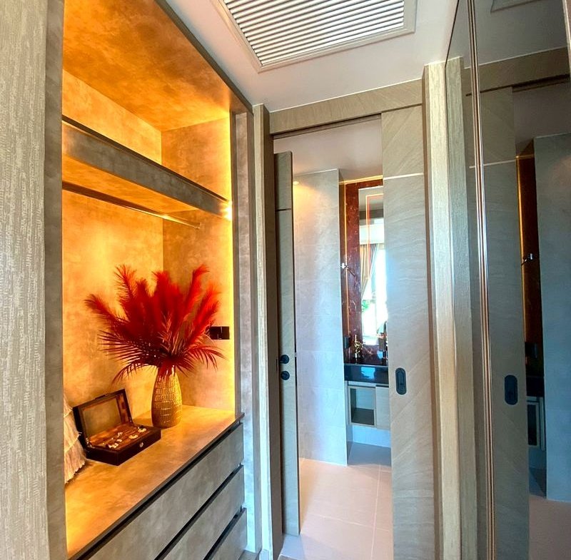 Luxurious hallway with warm amber lighting, a built‑in dresser, and a vase with red dried plumes on the counter.