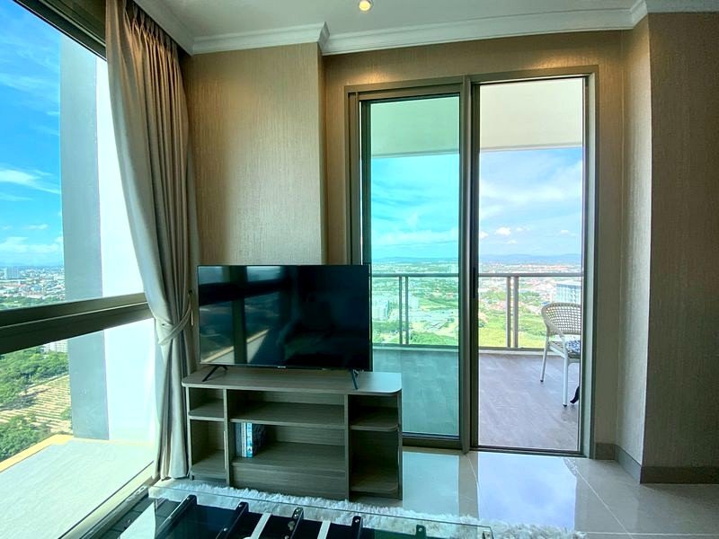 Living room with a TV on a small stand, glass doors to a balcony, and a panoramic city and green landscape view outside
