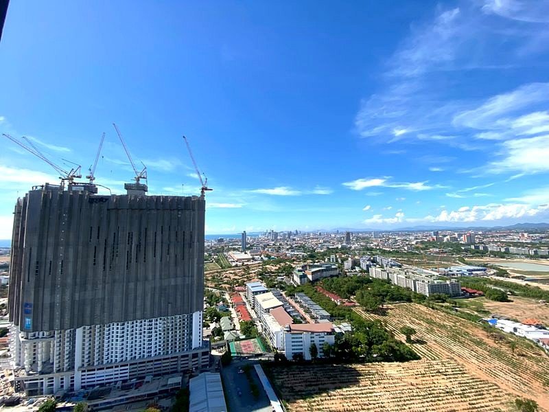 Tall under-construction high-rise with cranes on top overlooking a cityscape and blue sky.