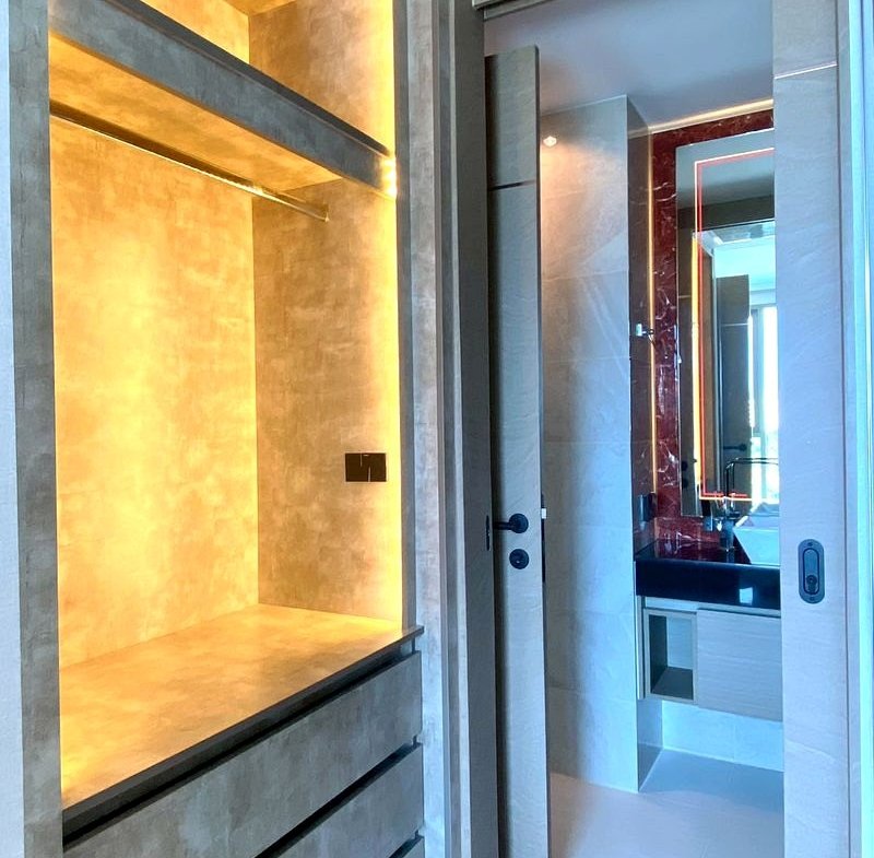 Modern walk-in closet with warm LED-lit display alcove, open shelves, and wide drawers, opening into a bathroom.