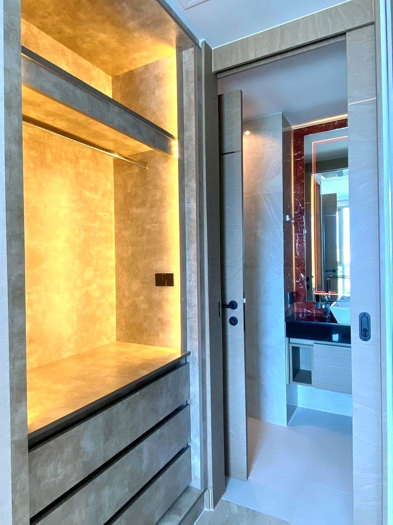 The_Riviera_Ocean_Drive_705_10 Modern walk-in closet with warm LED-lit display alcove, open shelves, and wide drawers, opening into a bathroom.