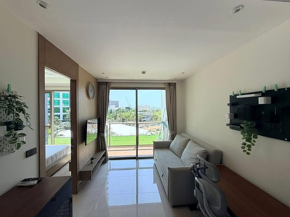 Modern living room with gray sofa facing a glass balcony door and a view of green lawn and city beyond.