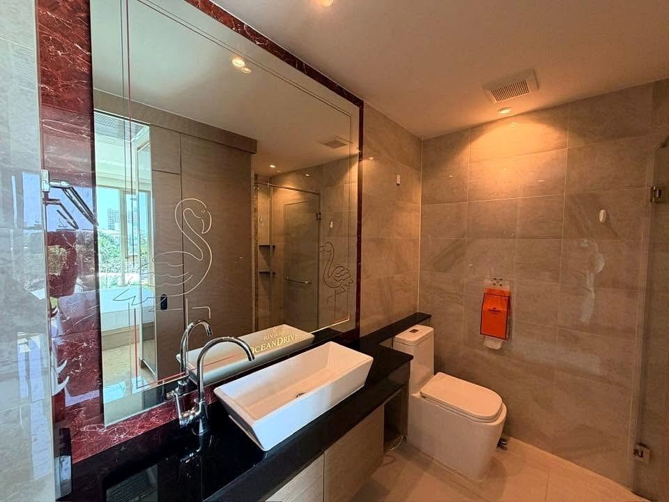 Contemporary bathroom with a white rectangular sink on a black countertop, large mirror with flamingo etching, and a toilet nearby.