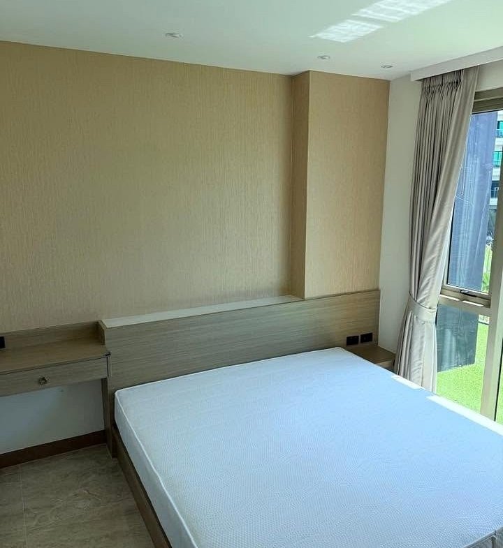 Bedroom in a modern hotel with a white mattress, light wood headboard, and built-in desk under beige wall panels.