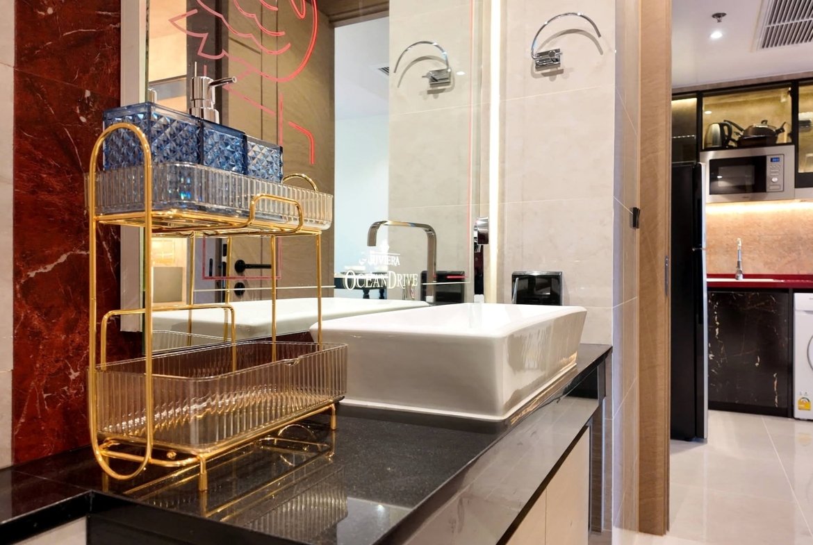 Luxurious modern laundry area with a gold metal cart beside a white sink, marble walls, and built‑in appliances in the background