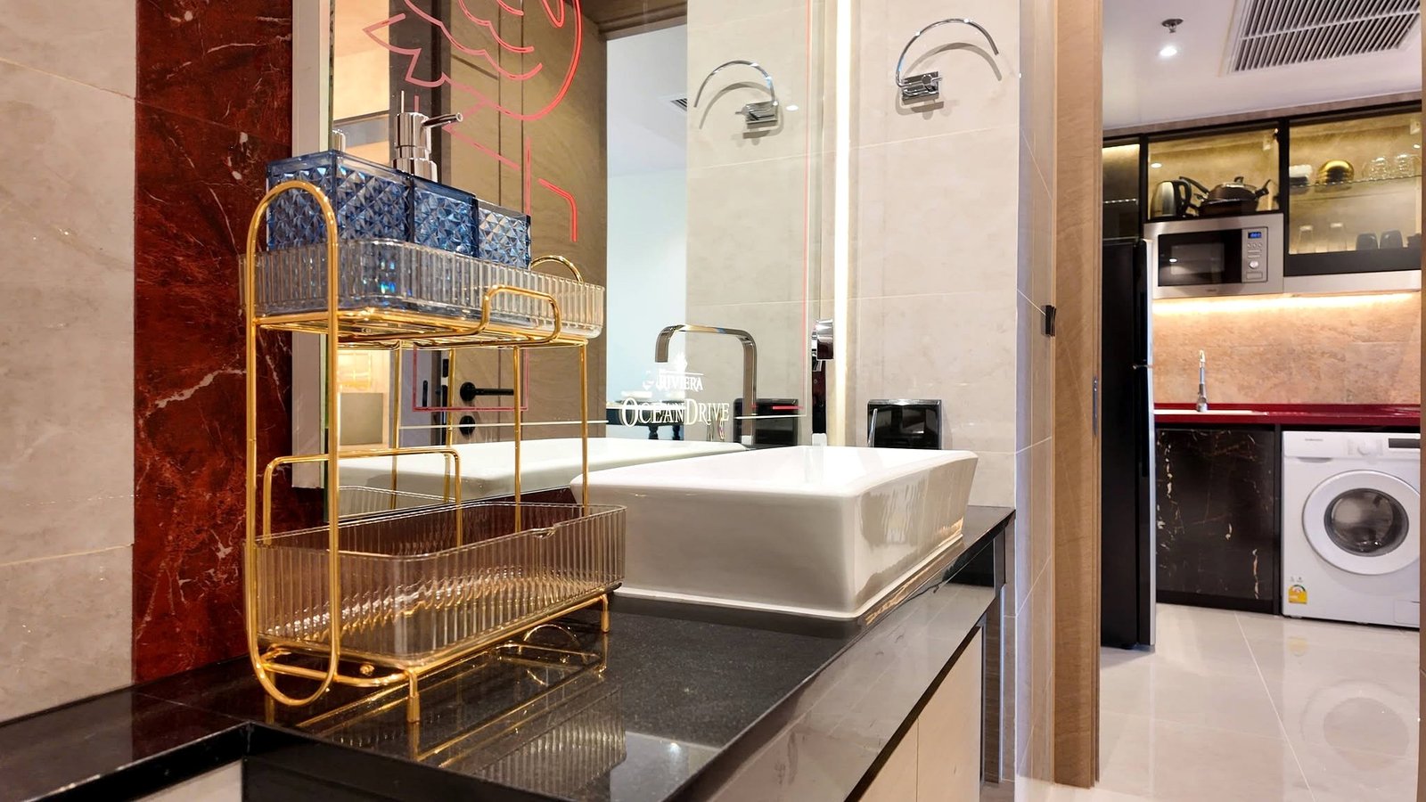 The_Riviera_Ocean_Drive_Pattaya_Dlc601_11 Luxurious modern laundry area with a gold metal cart beside a white sink, marble walls, and built‑in appliances in the background