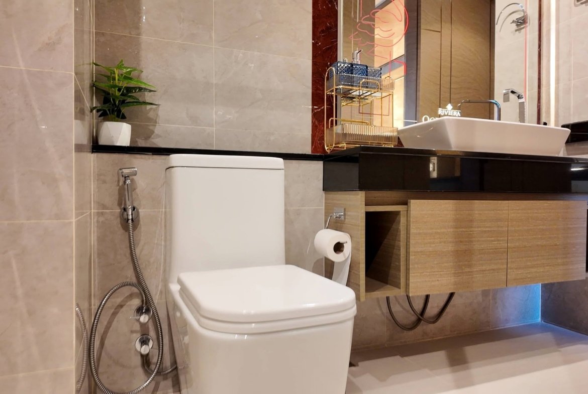 Modern bathroom featuring a white toilet, handheld bidet spray, and a dark wood vanity with a white rectangular sink and mirror above.