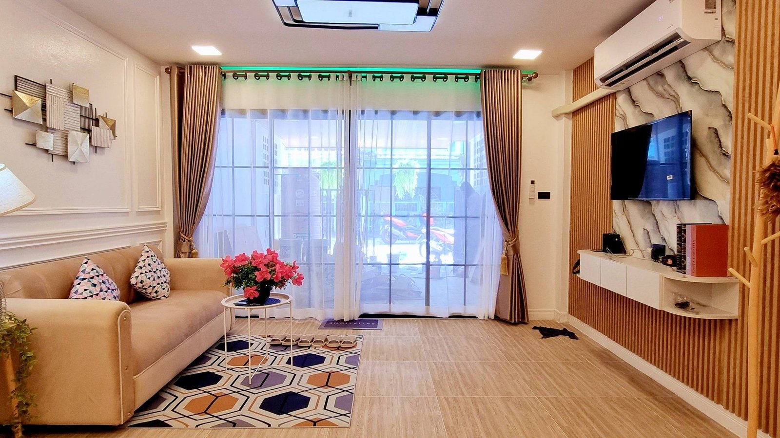 Town_home_Pattaya_Dlh551 Living room with beige sectional sofa, geometric rug, and pink flowers on a round glass table by large glass doors with sheer curtains.
