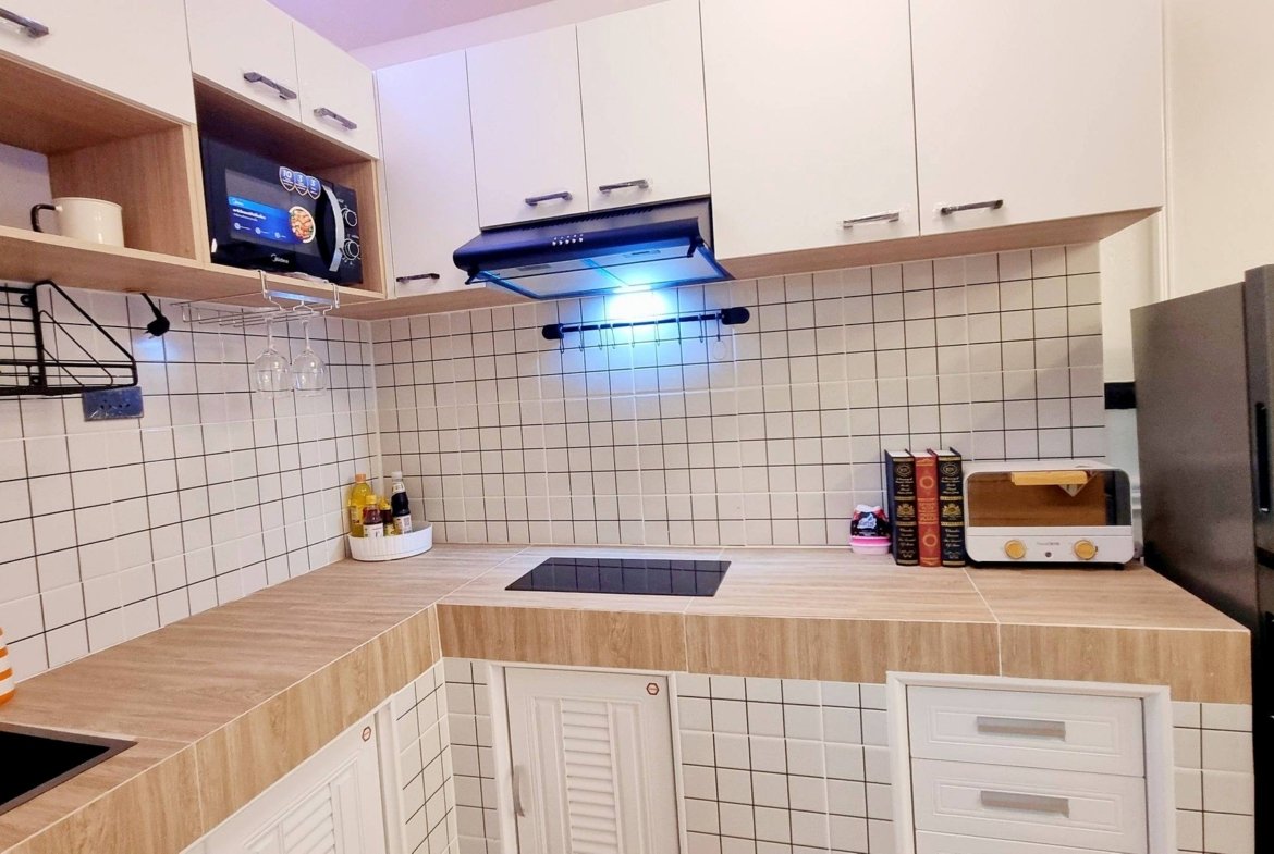Modern L-shaped kitchen with white cabinets, tiled backsplash, and wooden countertops; microwave, stove, and range hood visible.