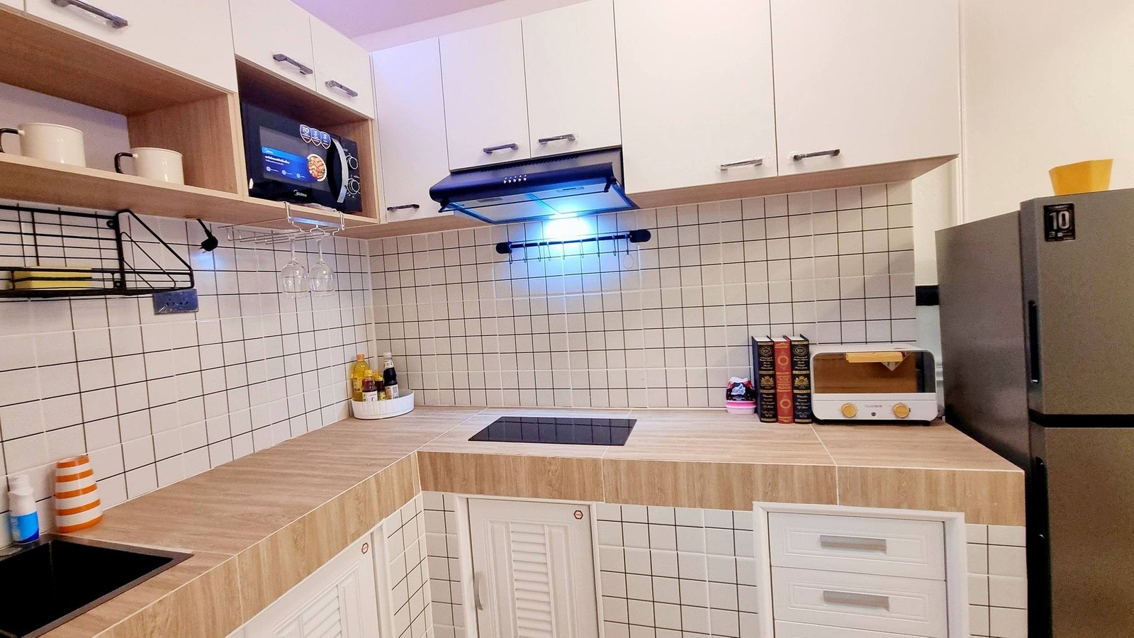 Town_home_Pattaya_Dlh551_11 Modern L-shaped kitchen with white cabinets, tiled backsplash, and wooden countertops; microwave, stove, and range hood visible.