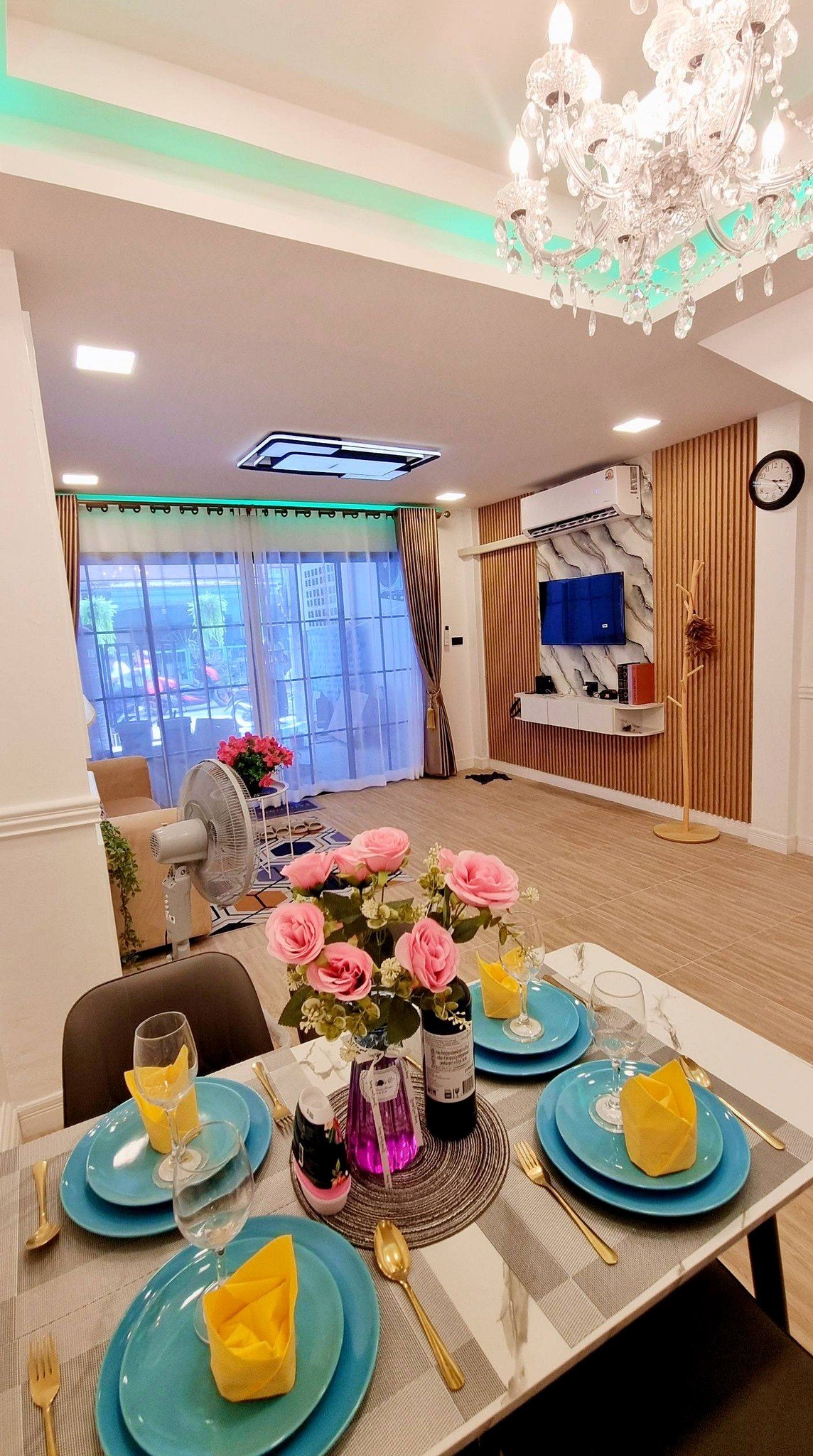 Town_home_Pattaya_Dlh551_2 Elegant dining table set for a meal with turquoise plates, yellow napkins, and pink roses; living room in background.
