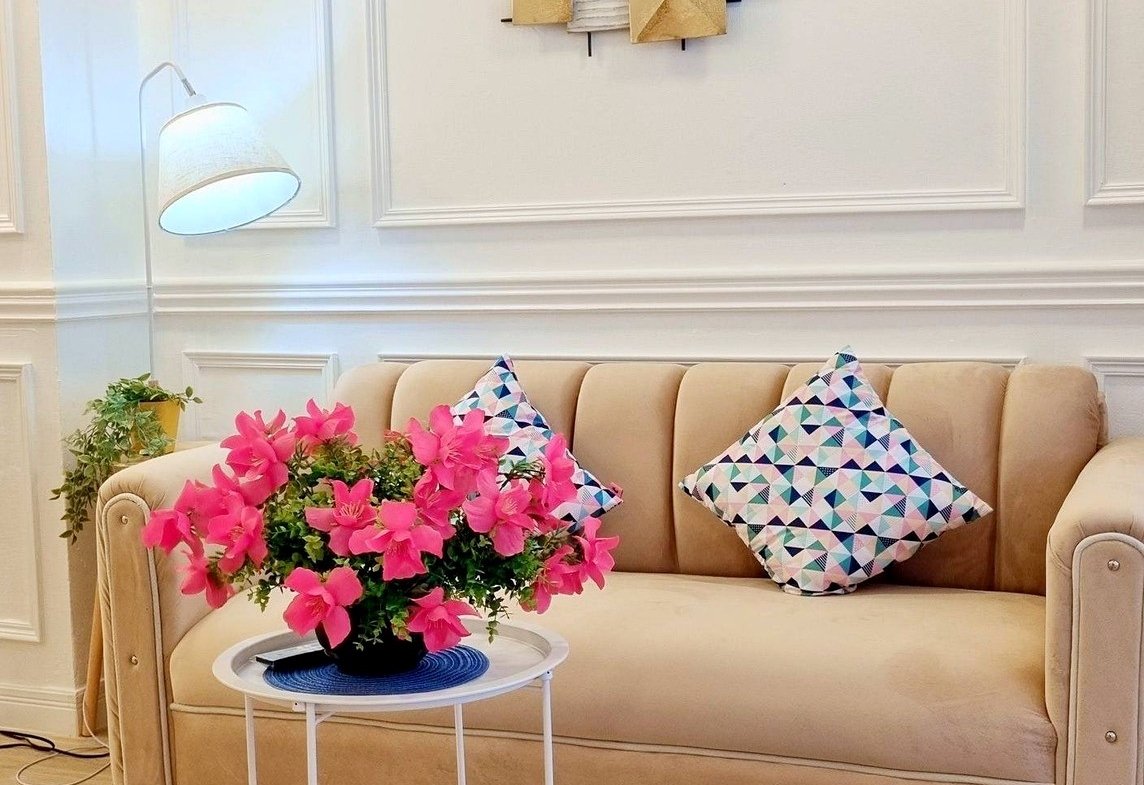 Beige sofa with geometric-patterned rug, pink flowers on a small table, and modern wall art in a bright living room.