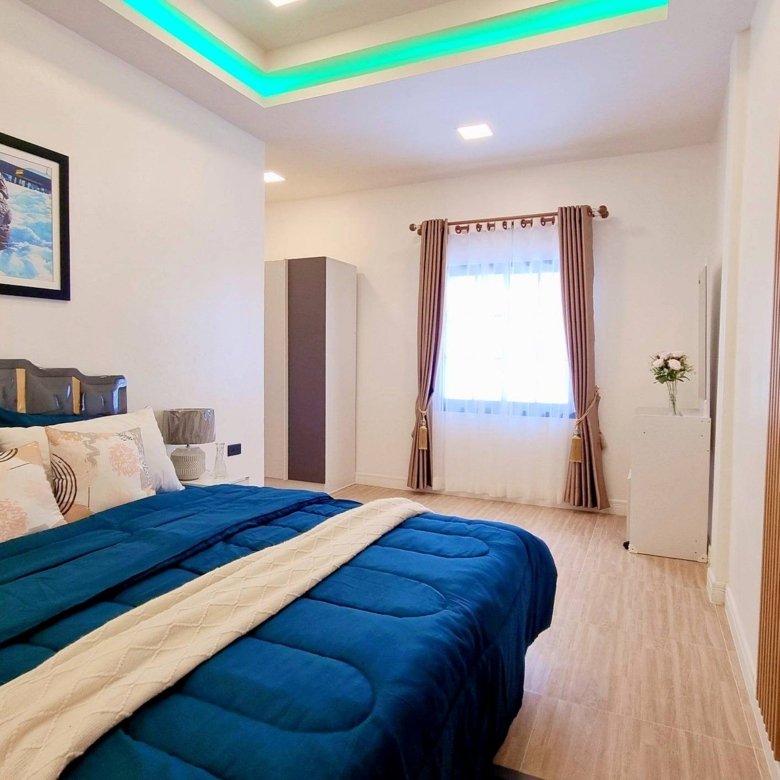 Bedroom with a large bed covered in a blue comforter and cream quilt decorative pillows and a framed photo on the wall