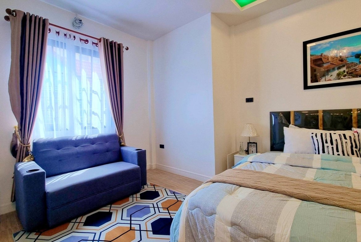 Twin beds in a bright hotel room with a blue sofa by the window and sheer curtains.