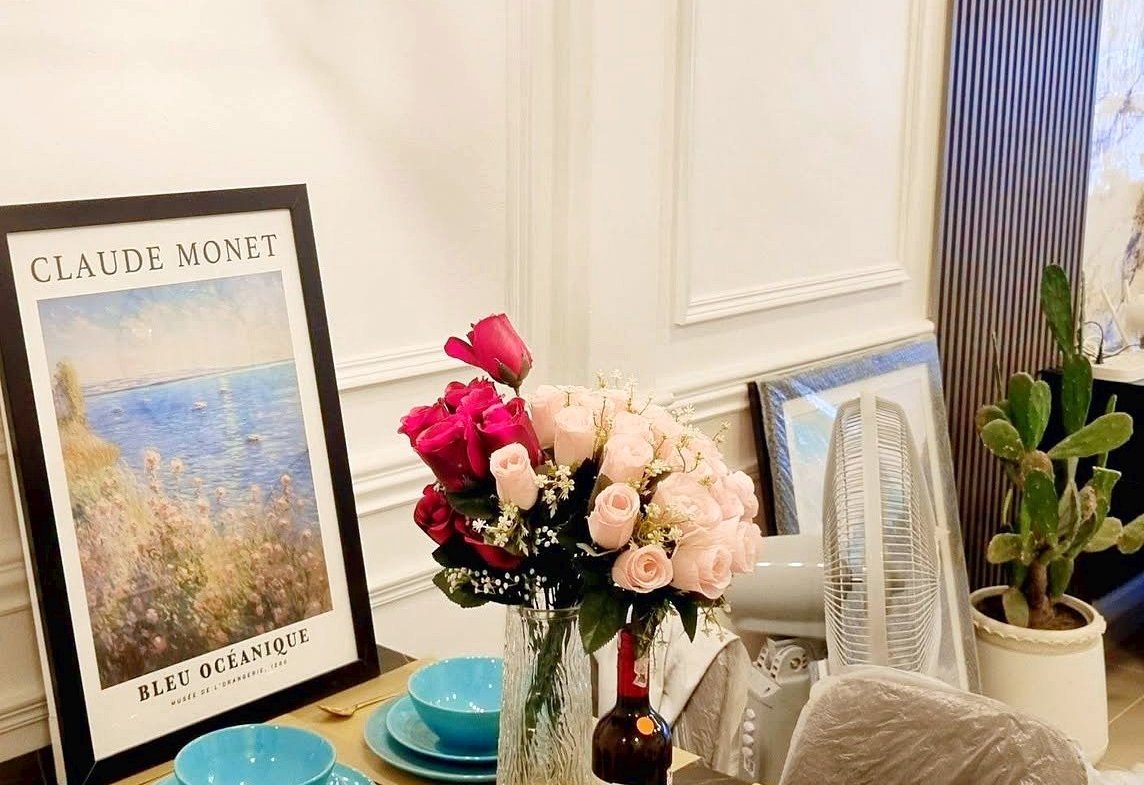 Dining table set with turquoise bowls, gold utensils, and a pink bouquet centerpiece under a geometric chandelier; Monet poster leaning on the wall in a stylish dining room.