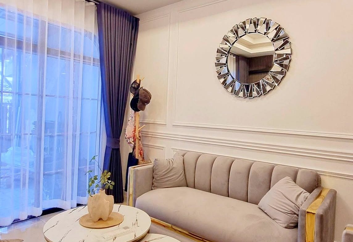 Elegant living room with a crystal chandelier, light beige sofa, and marble-top nesting tables on a geometric orange, gray, and black rug.