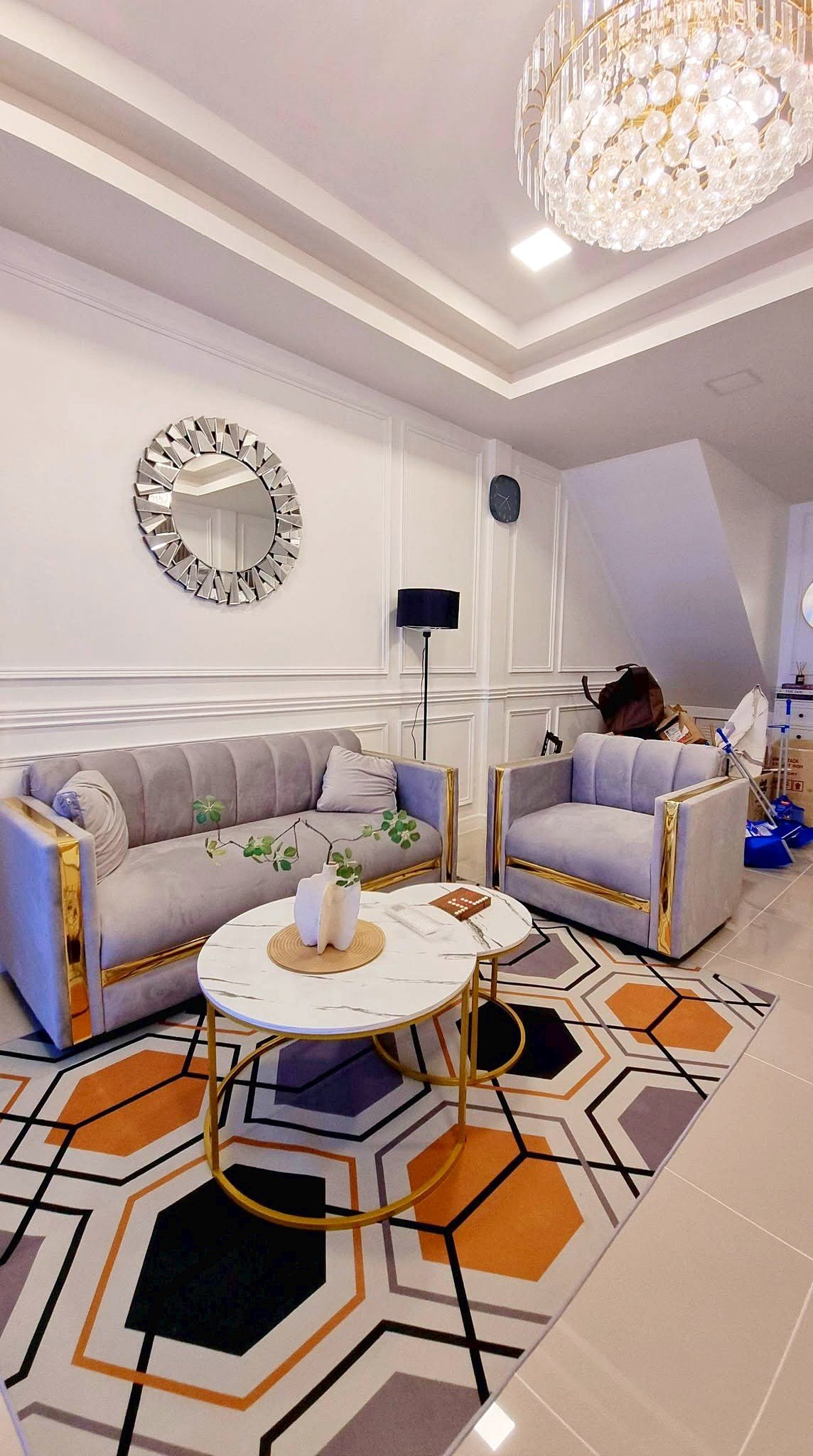 Townhome_South_Pattaya_Dlh581_15 Modern living room with gray velvet sofas and gold frames, white paneled walls, and a geometric orange-gray rug under round marble-topped coffee tables.