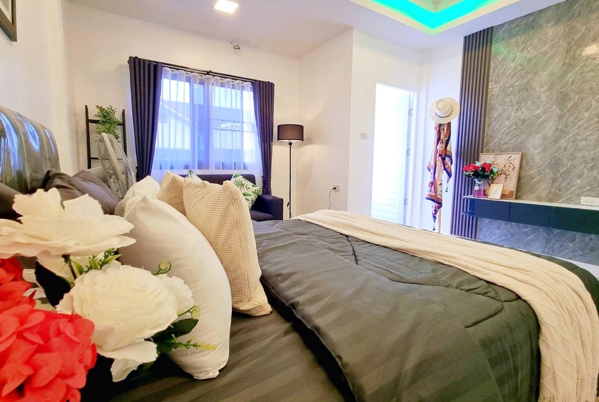 Cosy contemporary bedroom with two large beds, gray quilts, beige throws, and vibrant flowers in the foreground.