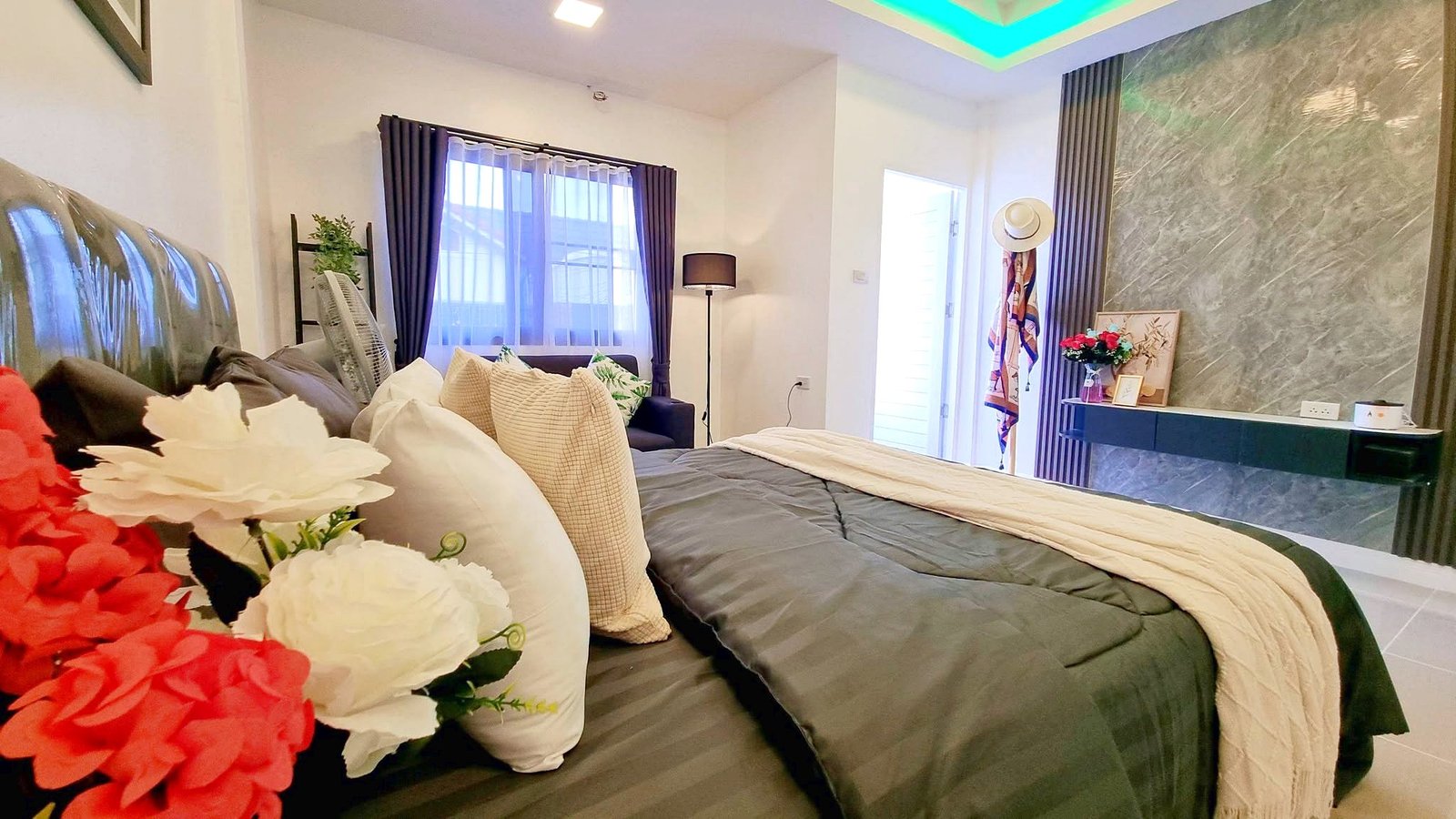 Townhome_South_Pattaya_Dlh581_18 Cosy contemporary bedroom with two large beds, gray quilts, beige throws, and vibrant flowers in the foreground.