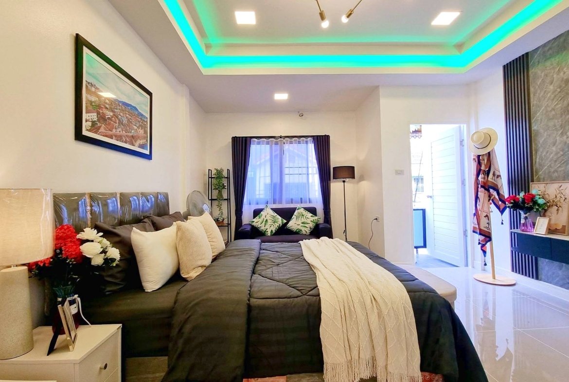 Bedroom with a large dark gray bed, cream throw, and plush pillows; white bedside table and lamp on the left side.