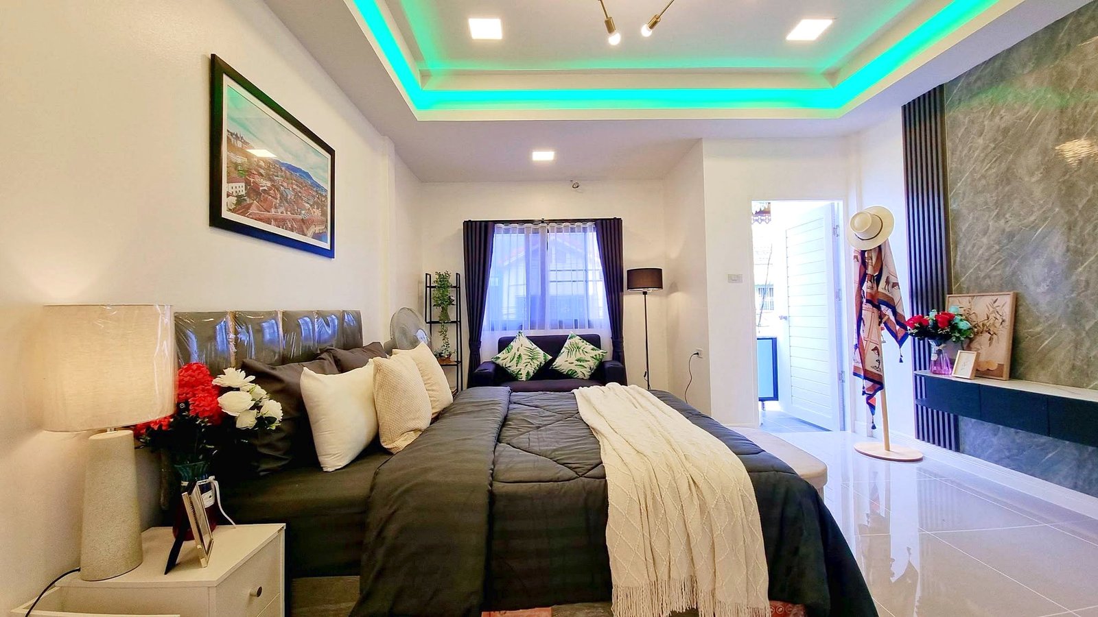 Townhome_South_Pattaya_Dlh581_3 Bedroom with a large dark gray bed, cream throw, and plush pillows; white bedside table and lamp on the left side.