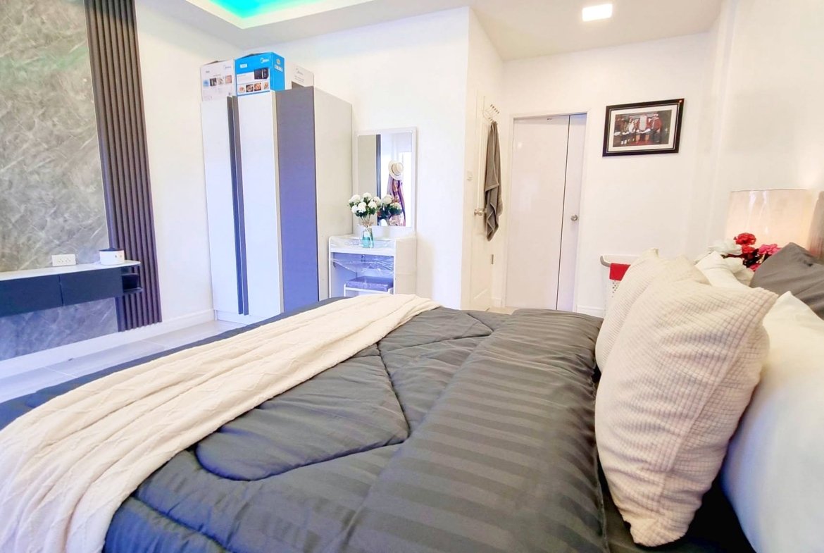 Large bed in a modern bedroom with gray striped bedding, a beige throw, and white pillows; marble accent wall and dresser with a mirror in the background.