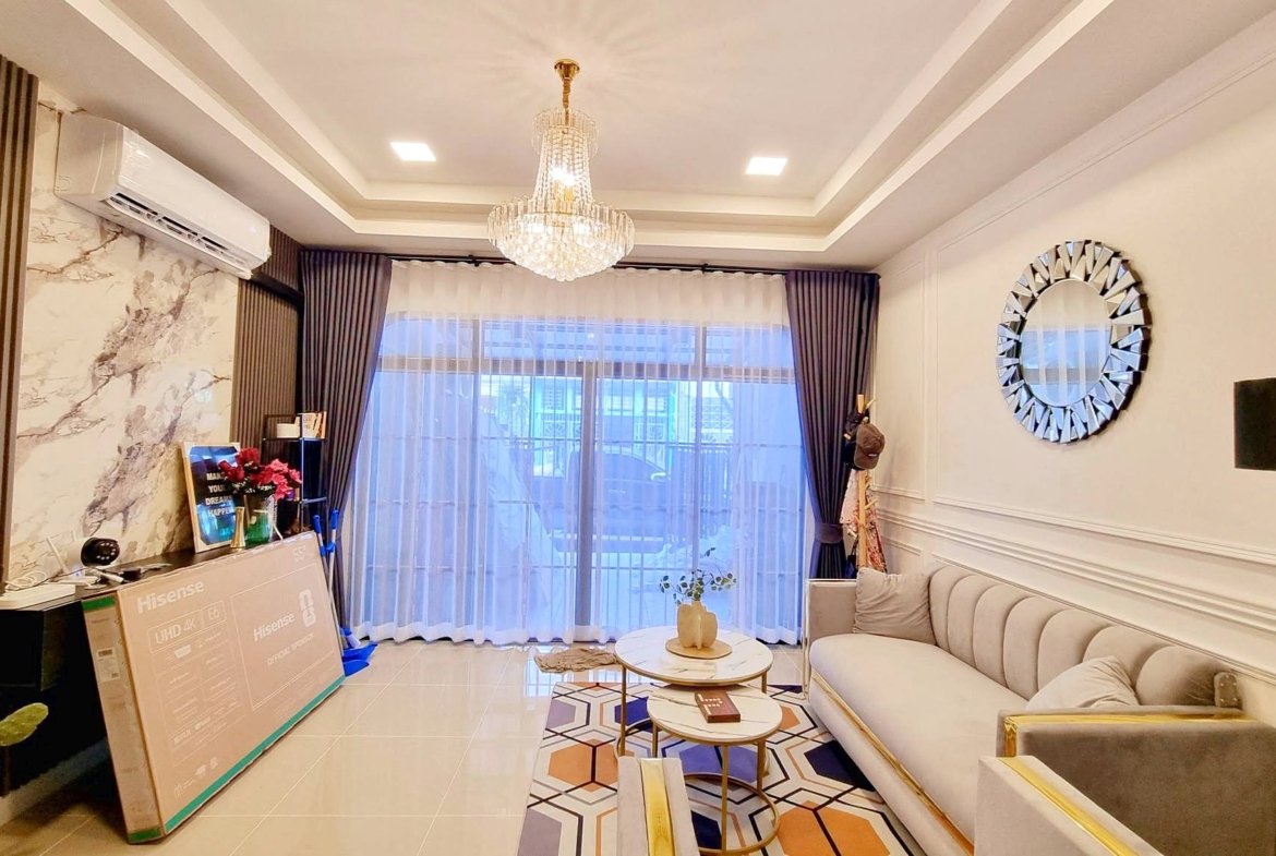 Living room with a crystal chandelier, large window with sheer curtains, and a light-gray sectional sofa.