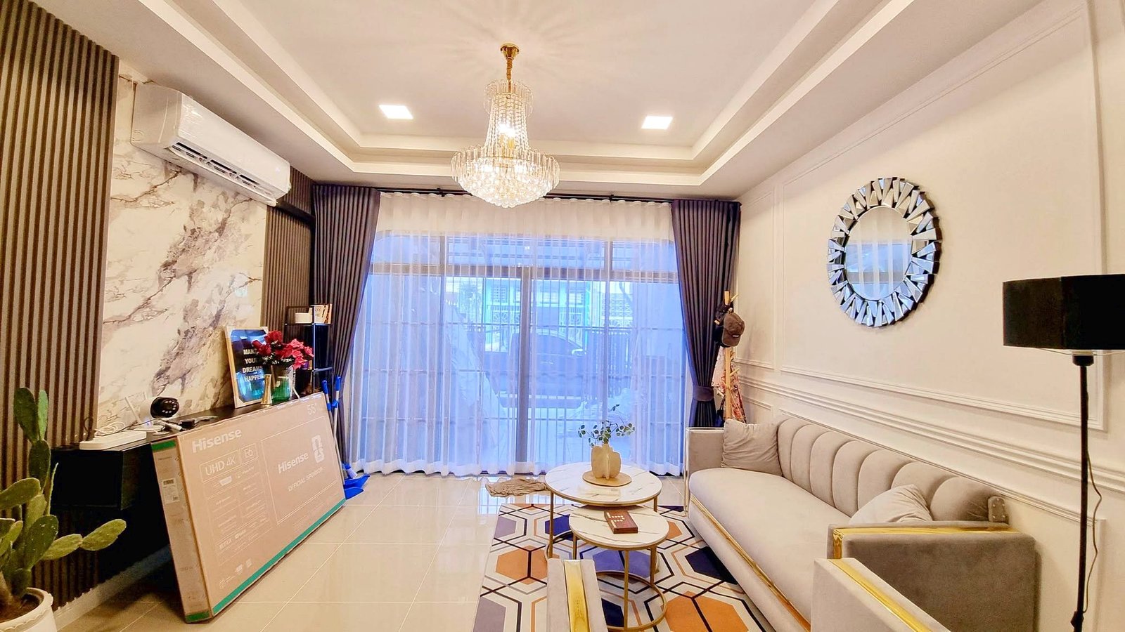 Townhome_South_Pattaya_Dlh581_6 Living room with a crystal chandelier, large window with sheer curtains, and a light-gray sectional sofa.