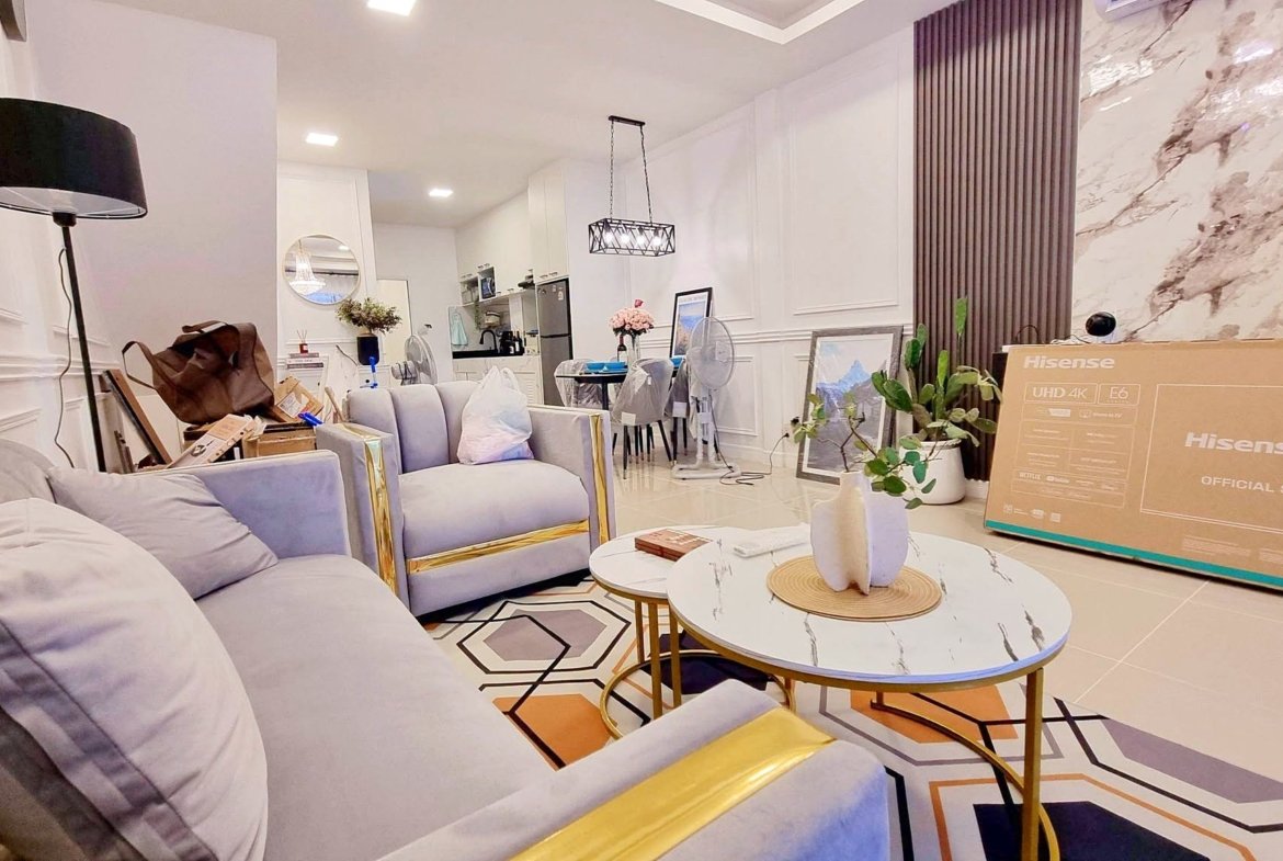 Bright modern living room with a gray sectional, round coffee tables, and a large Hisense TV box against a marble-walled backdrop.