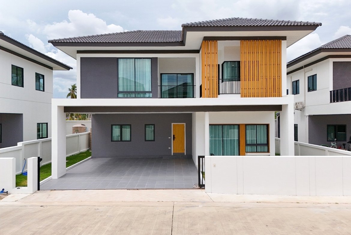 Modern two-story house with grey and white facade, wooden vertical slats, and a covered carport; bright yellow front door visible.
