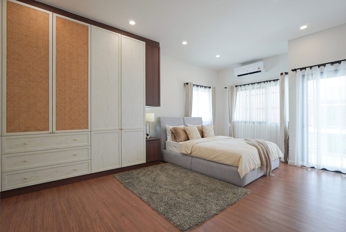 Bedroom featuring a large built-in wardrobe with woven panel doors, a gray upholstered bed, and bright windows with sheer white curtains.