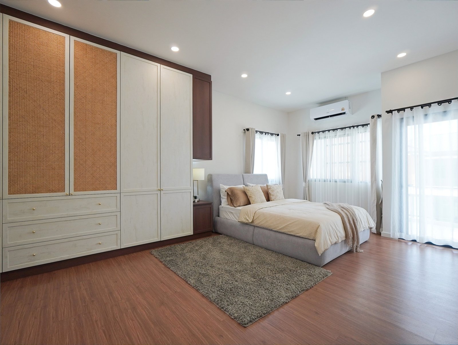 Tropical_Village_3_Pattaya_Dlh453_13 Bedroom featuring a large built-in wardrobe with woven panel doors, a gray upholstered bed, and bright windows with sheer white curtains.