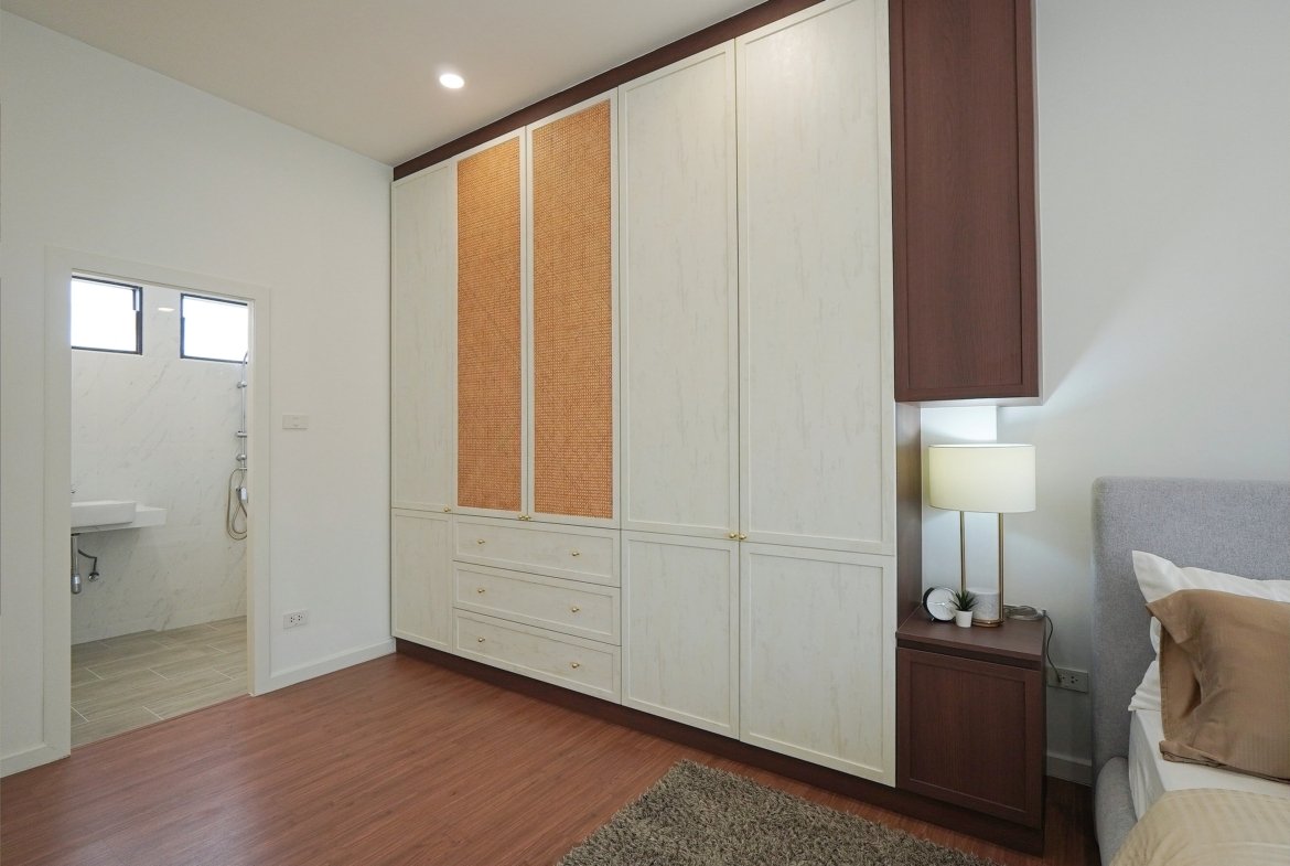 Bedroom with built-in cream wardrobes featuring woven panels and dark brown trim along the top, and a bedside lamp nearby.