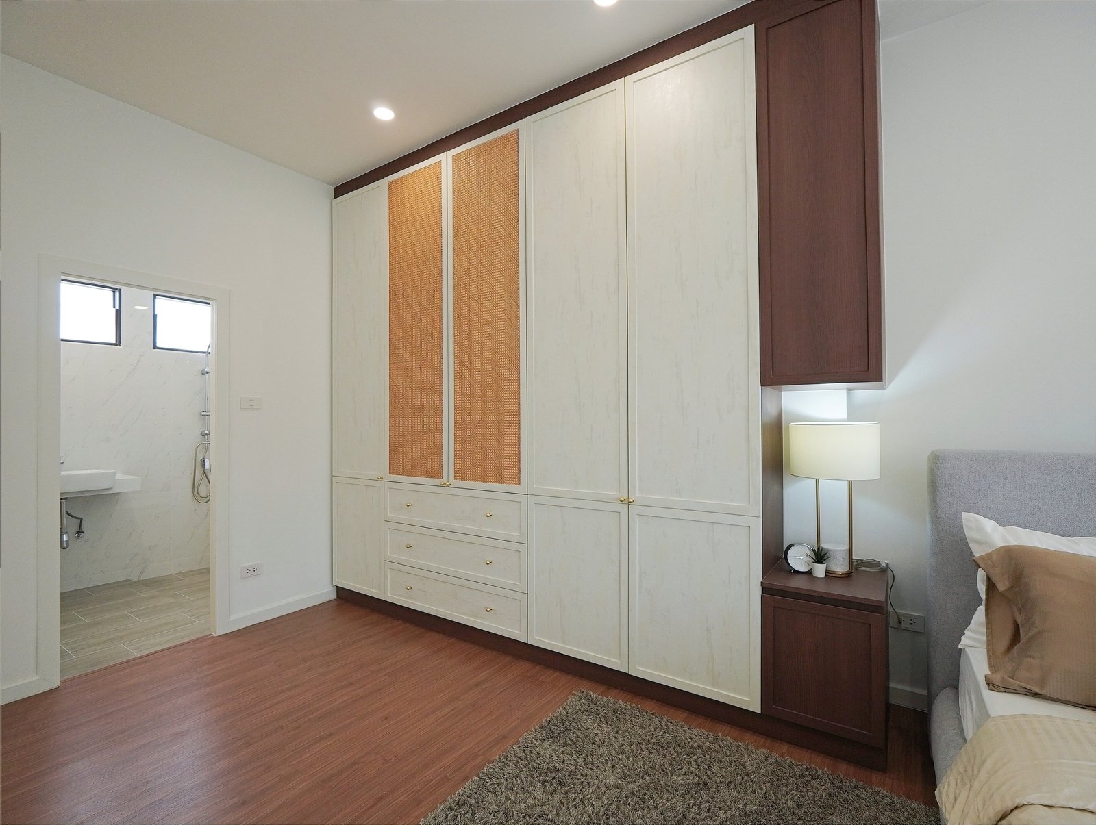 Tropical_Village_3_Pattaya_Dlh453_16 Bedroom with built-in cream wardrobes featuring woven panels and dark brown trim along the top, and a bedside lamp nearby.
