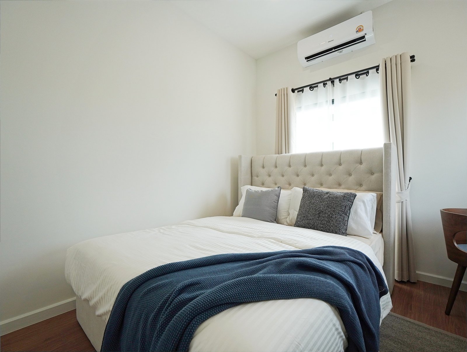 Tropical_Village_3_Pattaya_Dlh453_21 Neatly made bedroom with a tufted headboard bed, white bedding, and a navy blue throw blanket near the foot of the bed, window with beige curtains.
