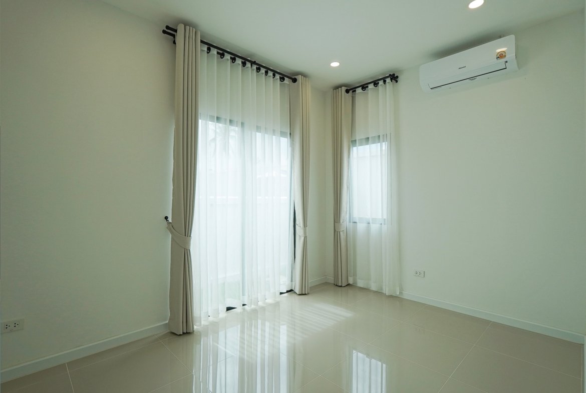 Bright empty room with large windows and sheer white curtains, reflecting light on a glossy tiled floor; wall-mounted air conditioner on the right.