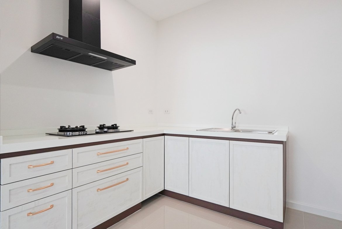 White modern kitchen with a black wall-mounted range hood above a gas cooktop and white cabinetry with copper handles