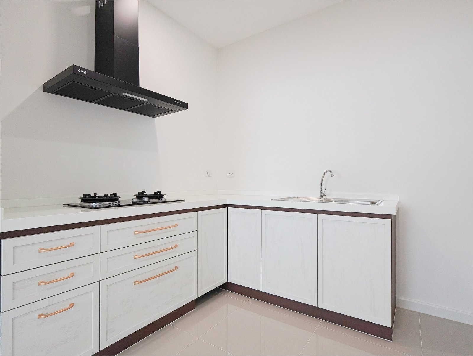 Tropical_Village_3_Pattaya_Dlh453_9 White modern kitchen with a black wall-mounted range hood above a gas cooktop and white cabinetry with copper handles