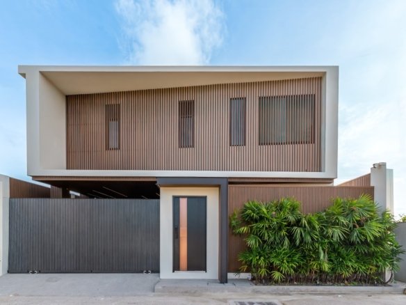 Modern two story house with wooden slat screen large entry door and tall black gate lush green bushes along the front right side