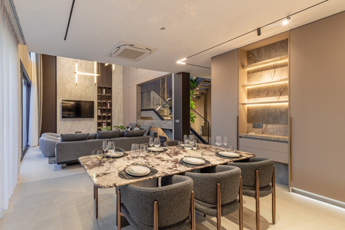 Open-plan dining and living room with a marble dining table set for eight, gray upholstered chairs, and a modern lounge area.