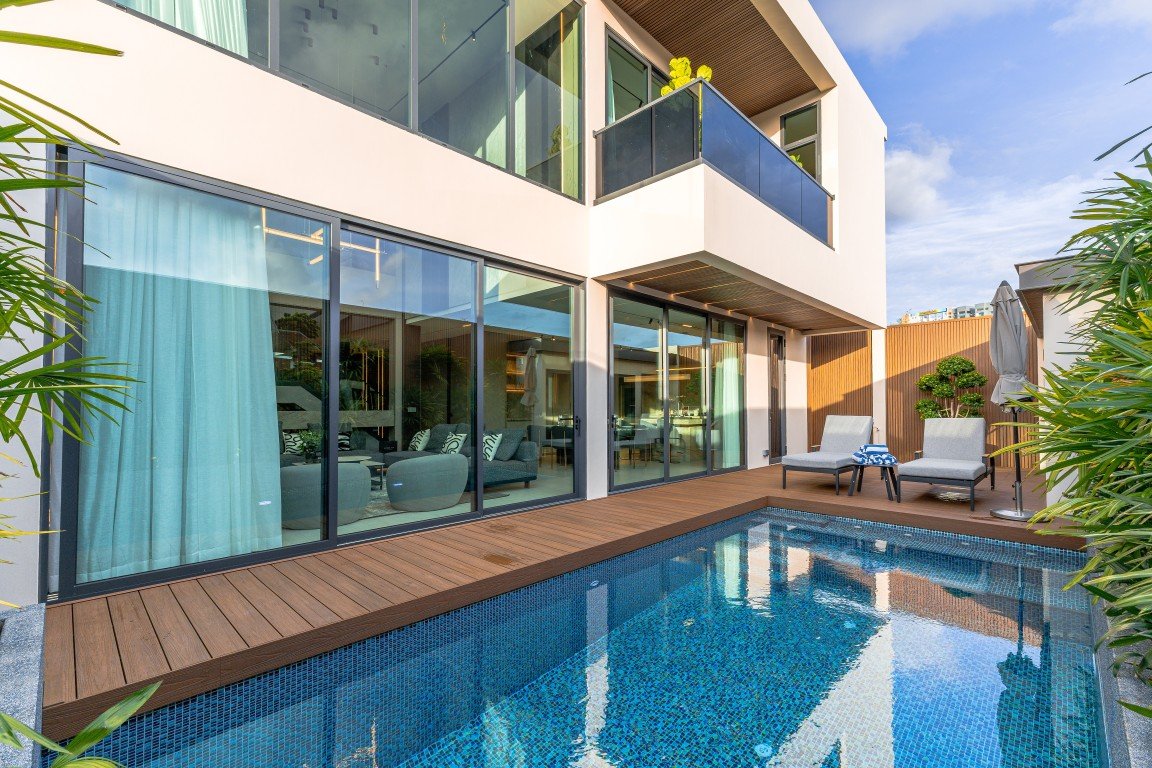 Modern two-story home with glass sliding doors and a blue-tiled rectangular pool on a wooden deck.