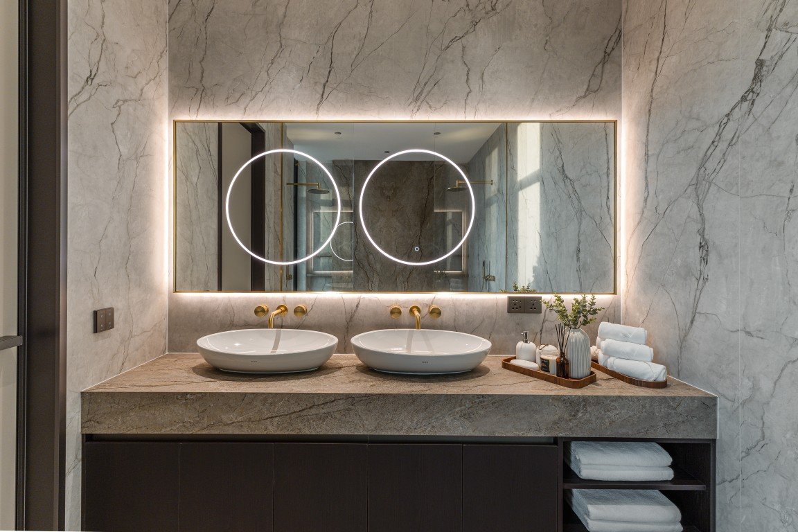 Double sink vanity with marble countertop, circular backlit mirrors, and gold faucets.